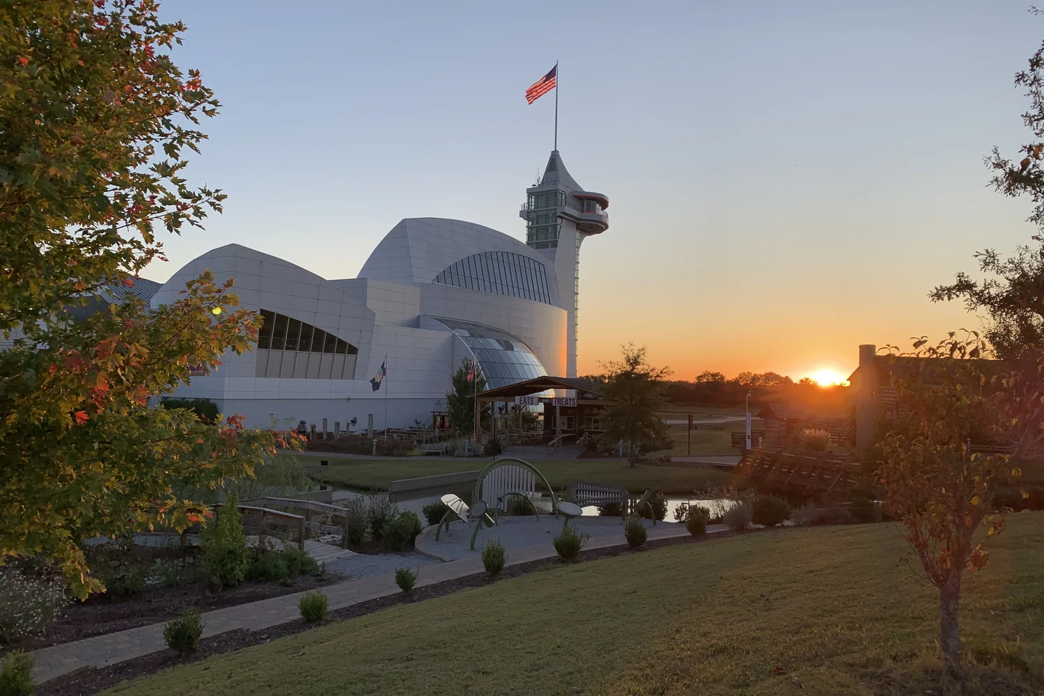 White curved museum buildings and observation tower at Discovery Park of America, with landscaped grounds at sunset.